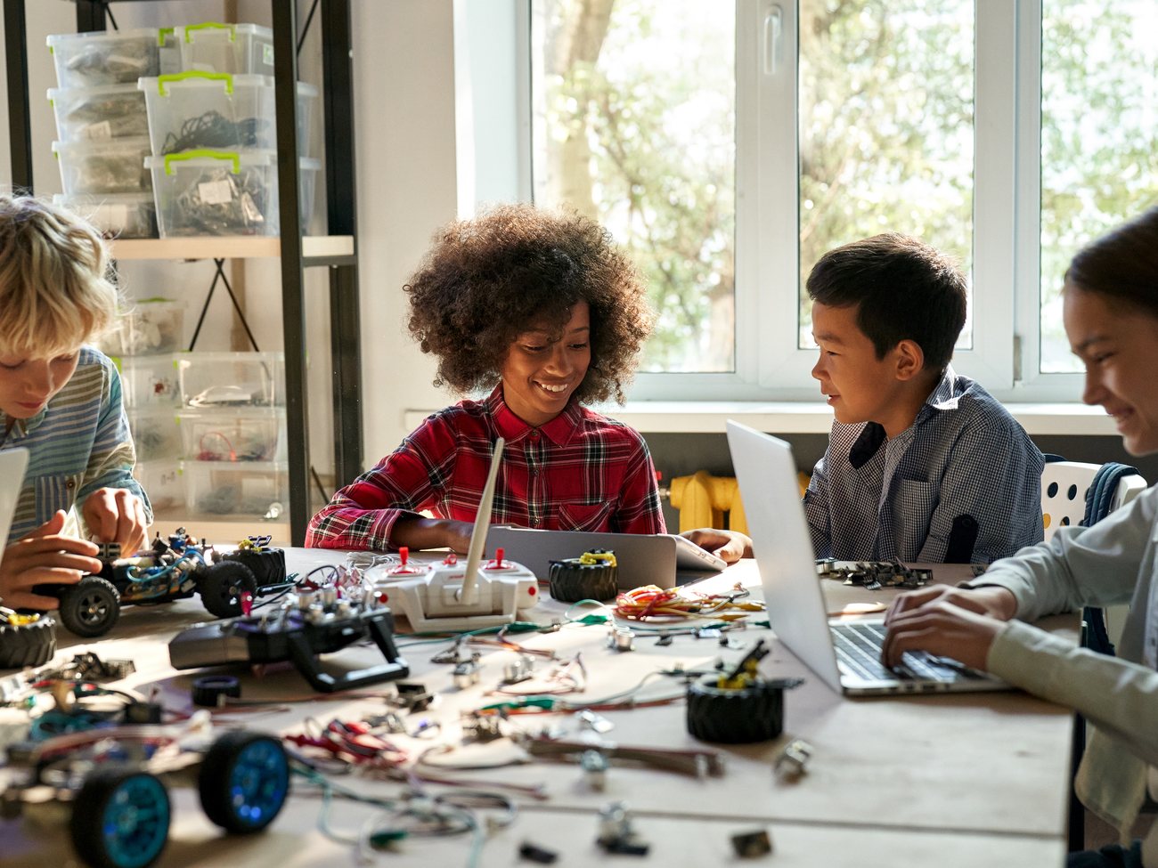 Students at a long table working on laptops and hardware projects together
