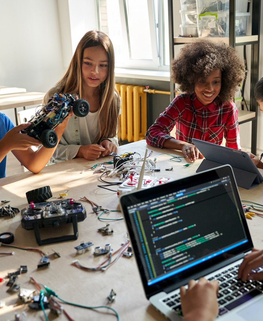 Students at a workbench of electronics projects with lines of code open on a laptop