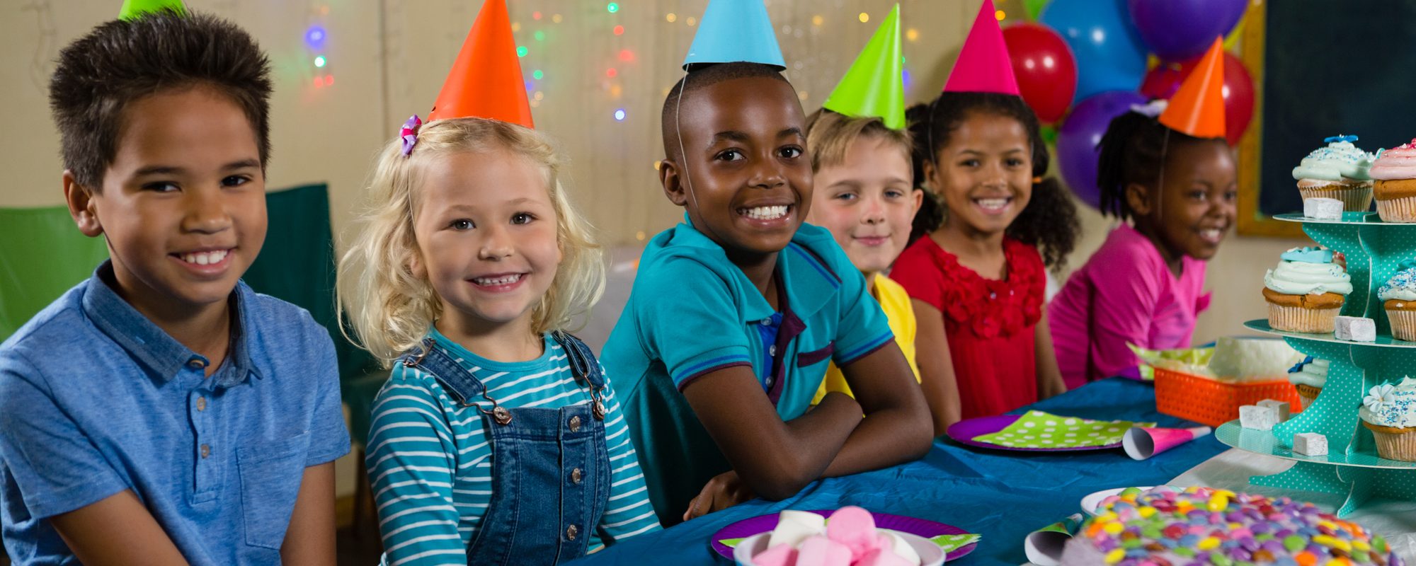 A group of children in party hats smiling around a birthday table