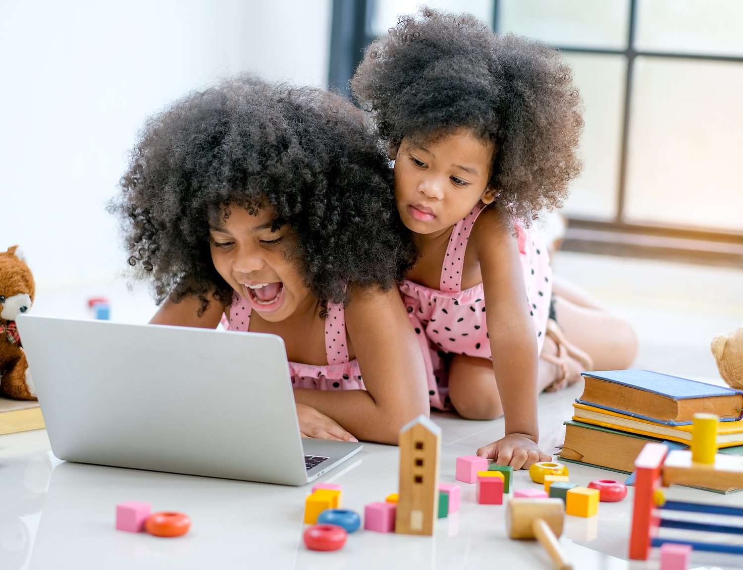 Two girls laughing at a laptop screen as they change a game they are building