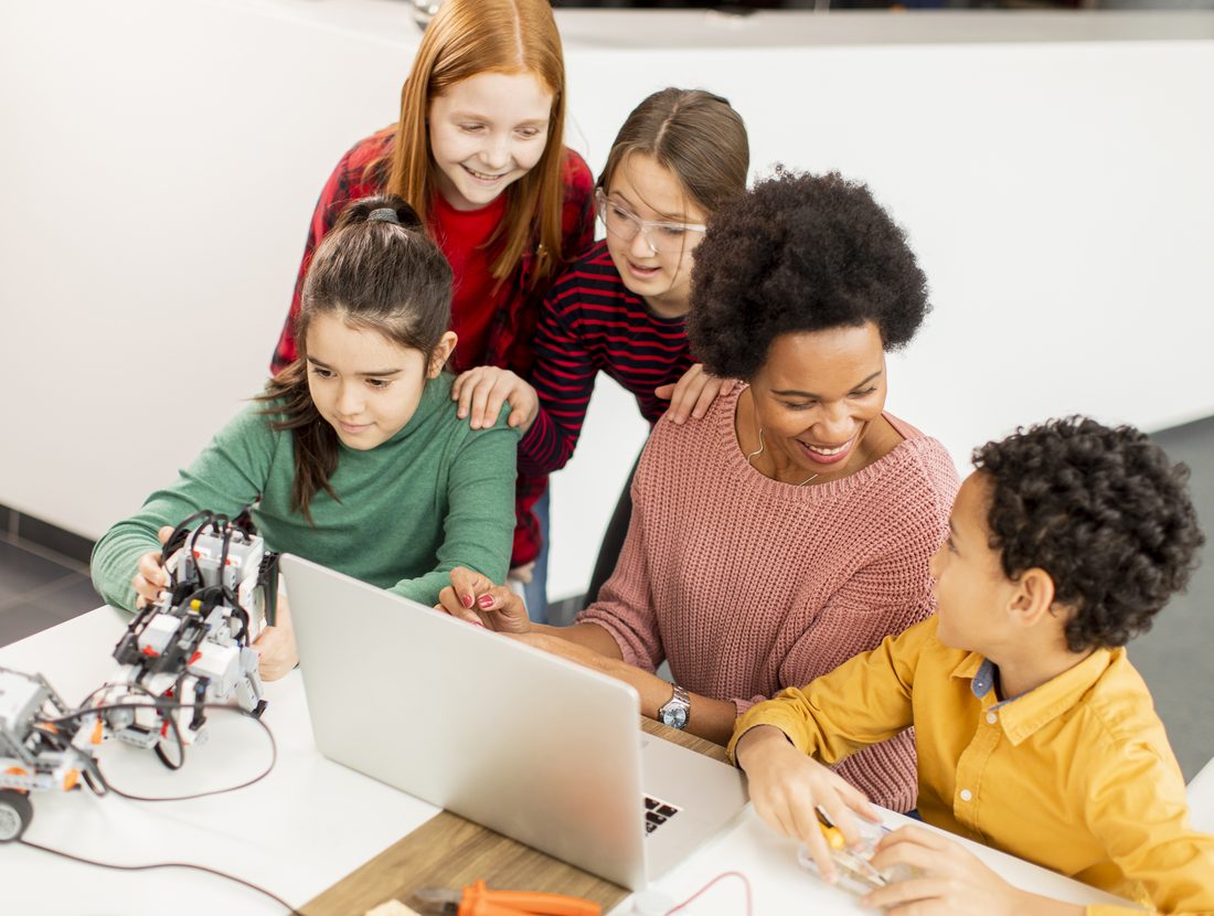 An instructor sitting beside children at a laptop, showing them where the code lives